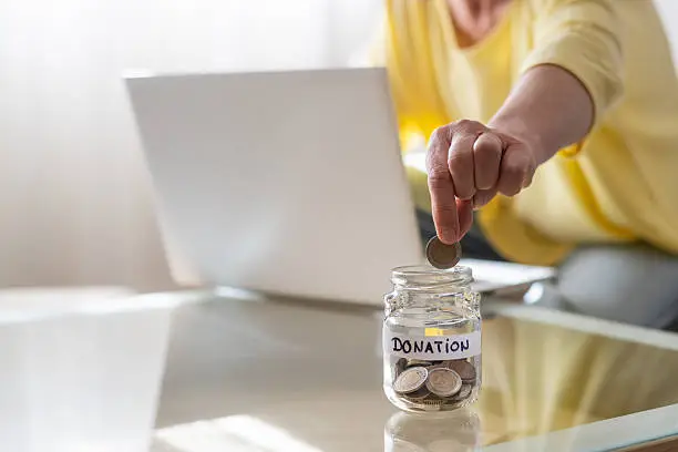 A donor dropping a coin into a donation jar beside a laptop